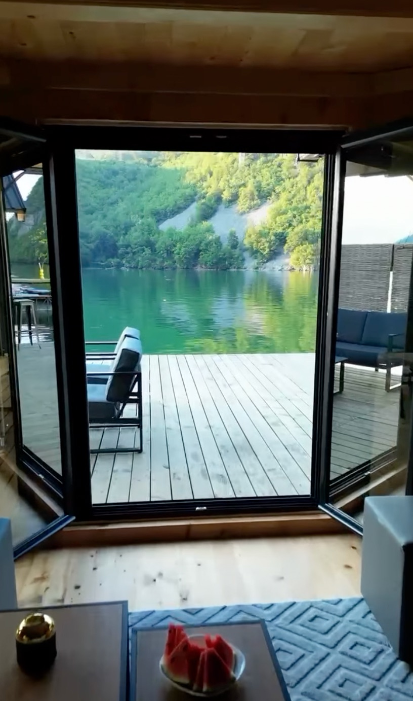 Pogled iz dnevnog boravka kroz otvorena staklena vrata na terasu i jezero